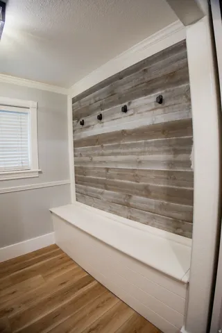 Built-in bench with storage, wood-finish flooring, wood plank accent wall, and built-in coat hooks