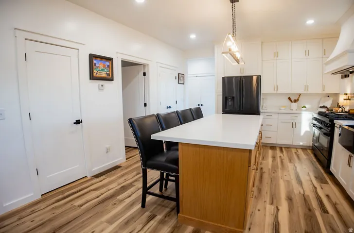 Spacious kitchen featuring an expansive center island with seating, ample white cabinetry, wood-finish flooring, and a contemporary pendant light fixture