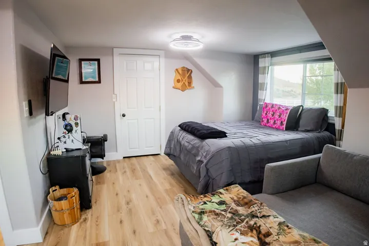 Wood-finish flooring, white paneled interior door, window with horizontal blinds, overhead ceiling light fixture, and sloped ceiling