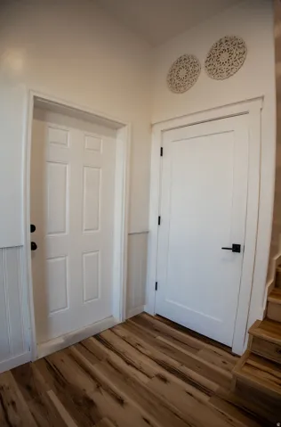 Wood-finish flooring with varying tones, beadboard wall paneling, and white doors with matte black hardware