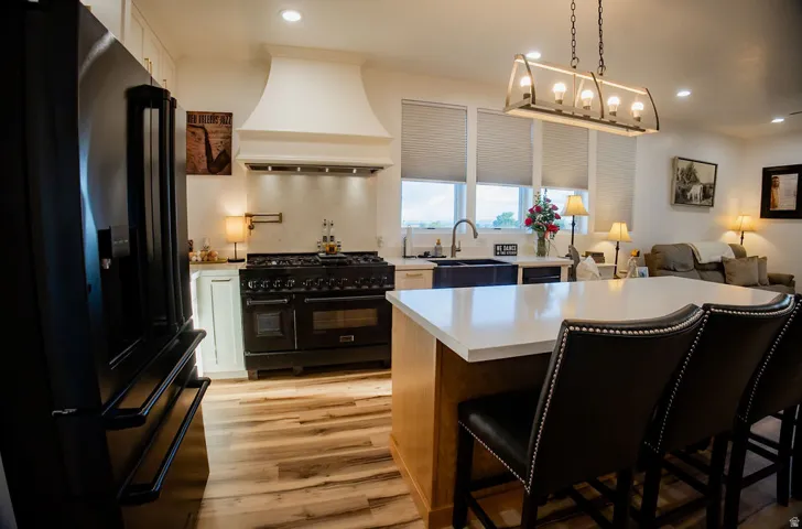 Open-concept kitchen with wood-finish flooring, a white countertop island with seating, a large black range, and white cabinetry
