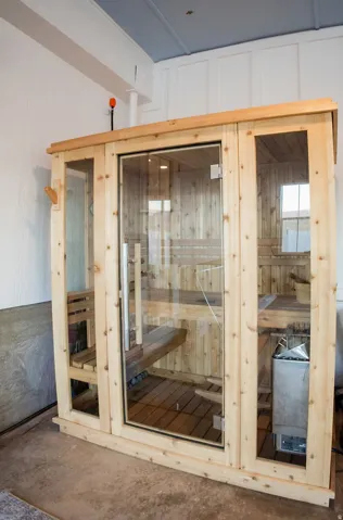 Wood-paneled sauna featuring a glass door, built-in benches, and a metal heater unit