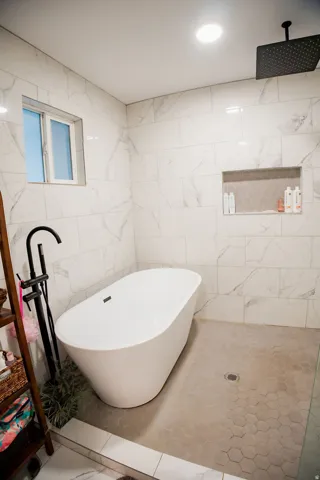 Freestanding soaking tub with a matte black floor-mounted faucet, tile walls, and a recessed shower niche with hexagonal tile