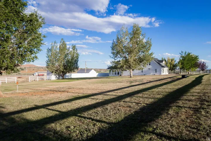 Expansive grassy area with a white picket fence, mature trees, and a distant white structure