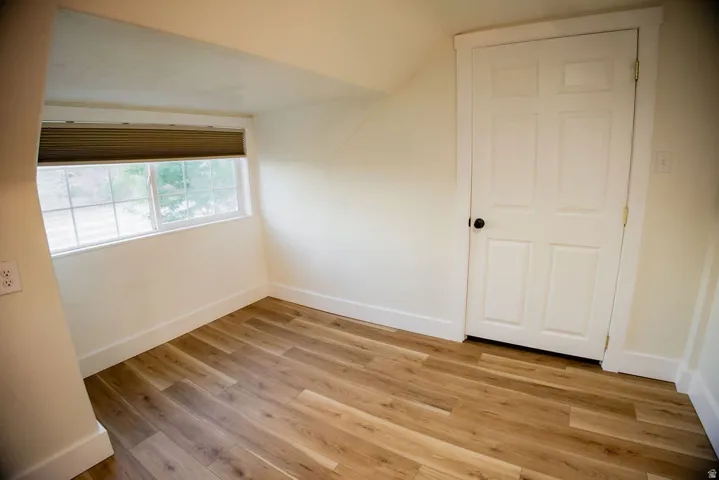 Light wood-finish flooring, white trim, and a white four-panel door with a black knob