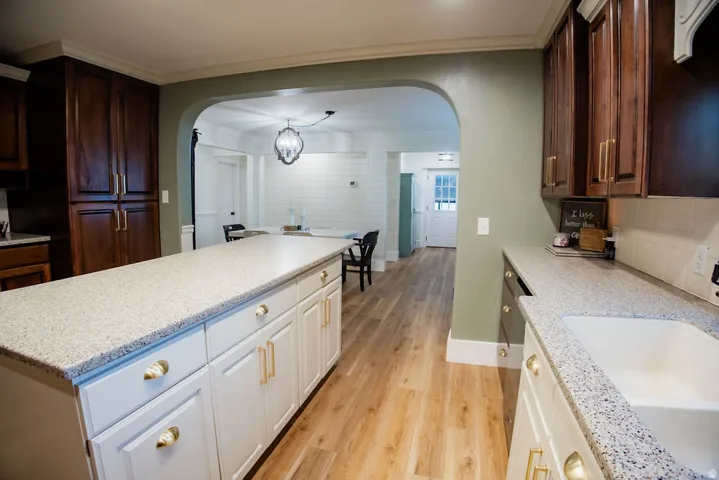Kitchen featuring wood-finish flooring, white shaker-style island cabinetry, light-toned countertops, and rich wood-finish upper cabinetry