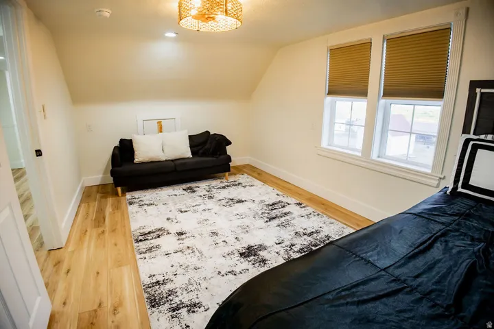 Attic space featuring wood-finish flooring, two windows with blinds, a woven light fixture, and recessed lighting