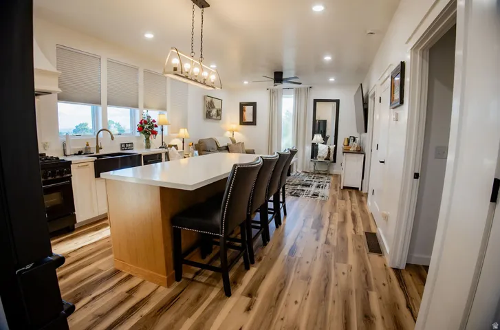 Open-concept living area featuring wood-finish flooring, a kitchen island with seating, recessed lighting, and a contemporary chandelier