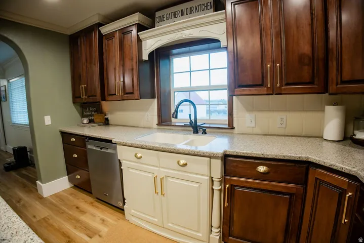 Wood-finish flooring, two-tone cabinetry, built-in dishwasher, composite double-basin sink with a matte black faucet, and speckled countertops