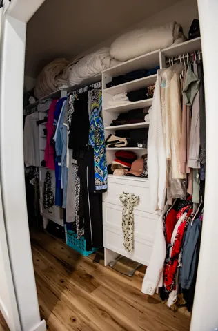 Walk-in closet featuring wood-finish flooring, white built-in shelving, hanging rods, and integrated drawers