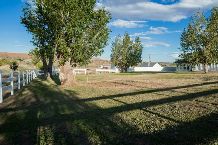 Expansive green space featuring a white split-rail fence, mature deciduous trees, and a distant white structure