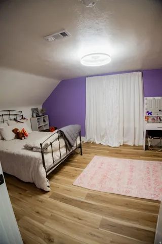 Wood-finish flooring, accent wall, modern ceiling light fixture, and white window coverings