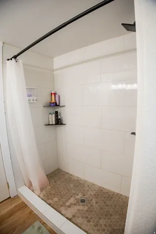 Shower with white subway tile surround, hexagon tile flooring, and integrated wall shelving