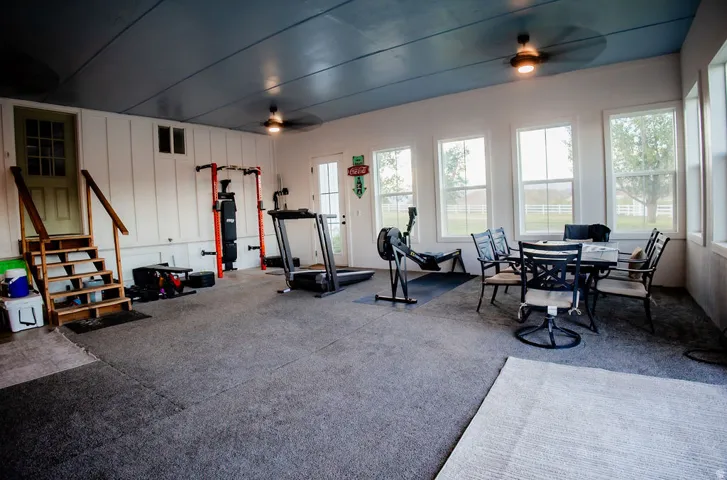 Spacious room with a paneled accent wall, multiple windows, and two ceiling fans