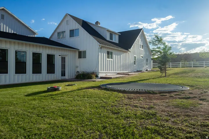 White board-and-batten siding with black-framed windows, dark roof, and a partial white fence in the background