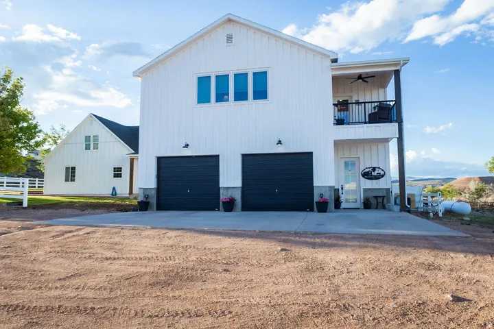 White board-and-batten exterior with a two-car garage, concrete driveway, and covered balcony