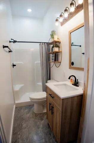 Shower with white surround, vanity with wood-finish cabinetry, white countertop, and gray-patterned flooring