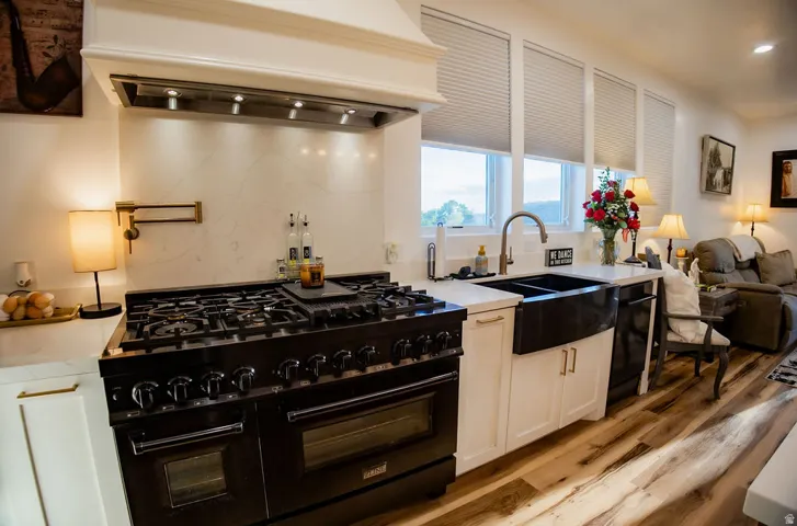 Stainless steel range with a pot filler, white cabinetry, quartz countertops, a farmhouse sink, and wood-finish flooring