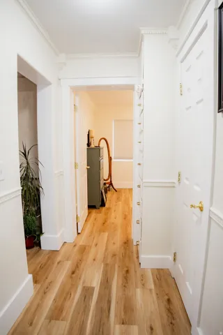 Wood-finish flooring throughout, white crown molding, white doors with brass hardware, and white wall paneling