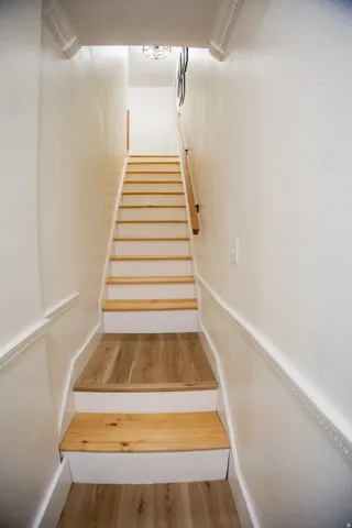 Staircase featuring wood-finish treads and risers, white walls, decorative molding, and a built-in handrail
