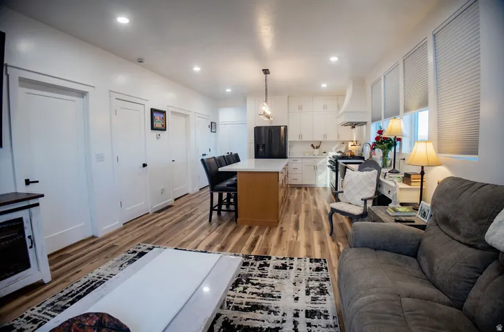 Open-concept living area featuring wood-finish flooring, recessed lighting, a kitchen island with seating, and white kitchen cabinetry