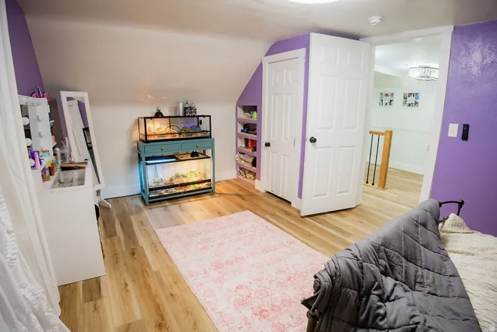 Wood-finish flooring, white paneled door, built-in shelving, sloped ceiling, recessed lighting