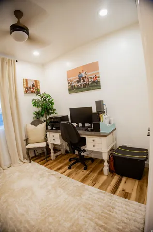 Recessed ceiling lighting, wood-finish flooring, ceiling fan with integrated light, white walls, and a window with drapes