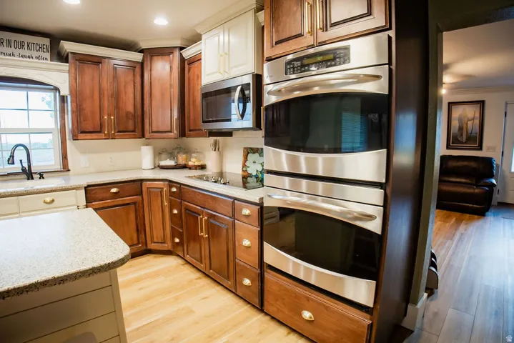 Two-tone cabinetry with gold-tone hardware, stainless steel appliances, light-toned wood-finish flooring, and light-toned countertops