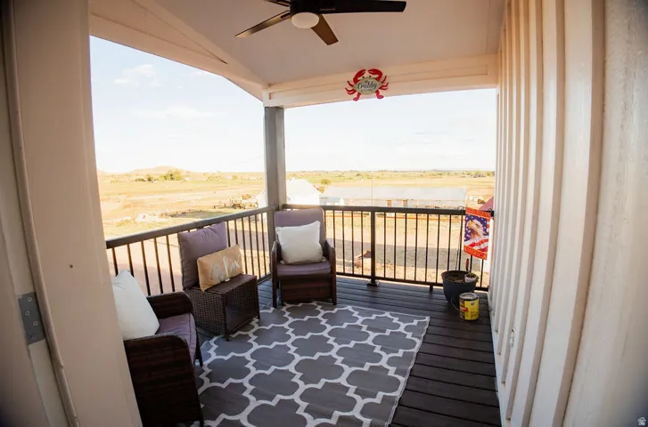 Covered balcony featuring a ceiling fan, dark wood-finish decking, and metal railings