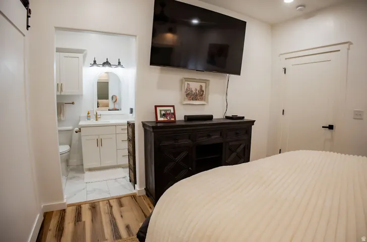 Wood-finish flooring leading to an en-suite bathroom with white cabinetry, a vanity with a white countertop, and a toilet