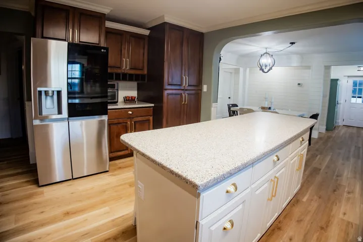 Kitchen featuring wood-finish flooring, a central island with a light-toned countertop, white cabinetry with gold-tone hardware, and dark wood-tone perimeter cabinetry