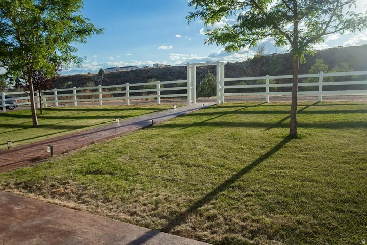 Manicured lawn, paved walkway, white fence, decorative archway, and mature trees