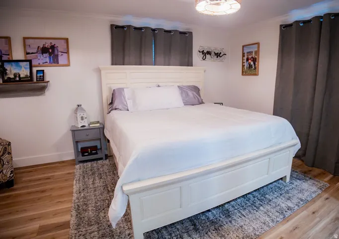 Wood-finish flooring with white baseboards, crown molding, and white walls