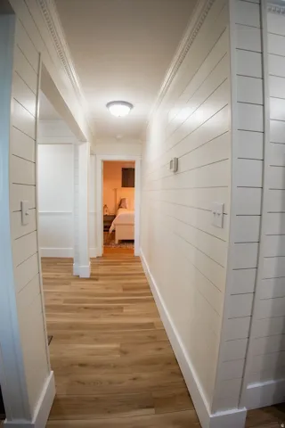 Hallway featuring wood-finish flooring, white shiplap walls, white crown molding, white baseboards, and a flush-mount ceiling light