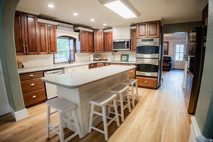 Kitchen with wood-finish flooring, white shiplap island with seating, integrated dishwasher, double wall ovens, and wood cabinetry with stainless steel appliances