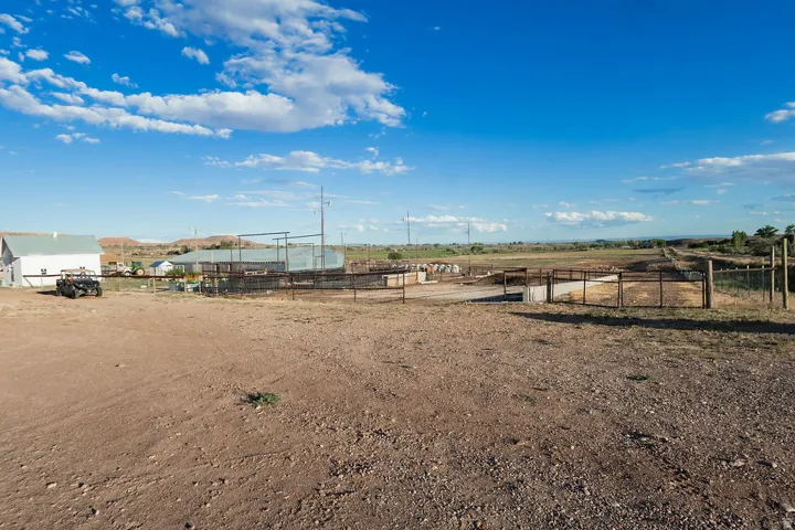 Expansive property featuring a white outbuilding, multiple fenced enclosures, and a broad open field