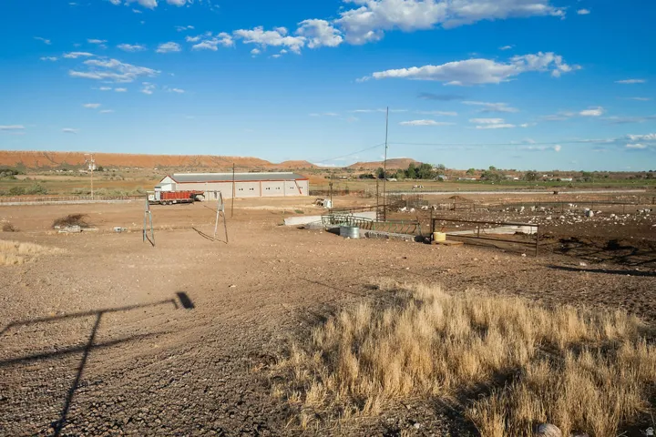 Expansive open land featuring a large building with multiple windows, fenced enclosures, and a prominent red soil backdrop
