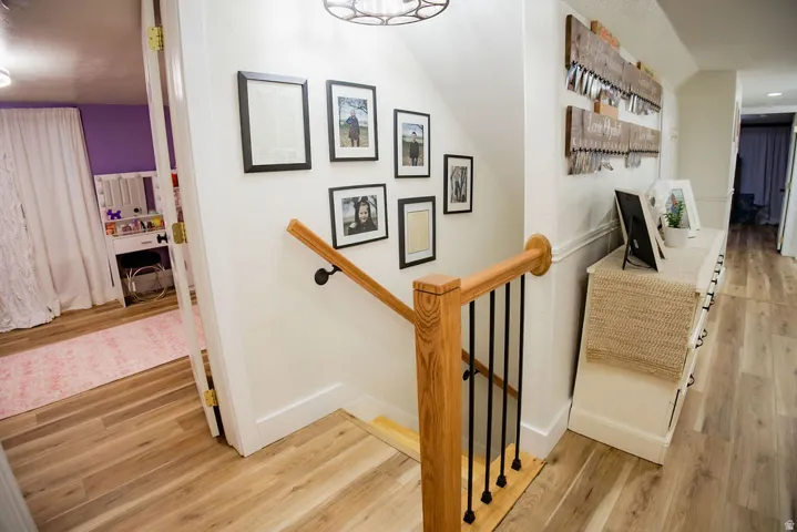 Wood-finish flooring throughout, white wall paneling, natural wood handrail, black metal balusters, and a modern ceiling light fixture