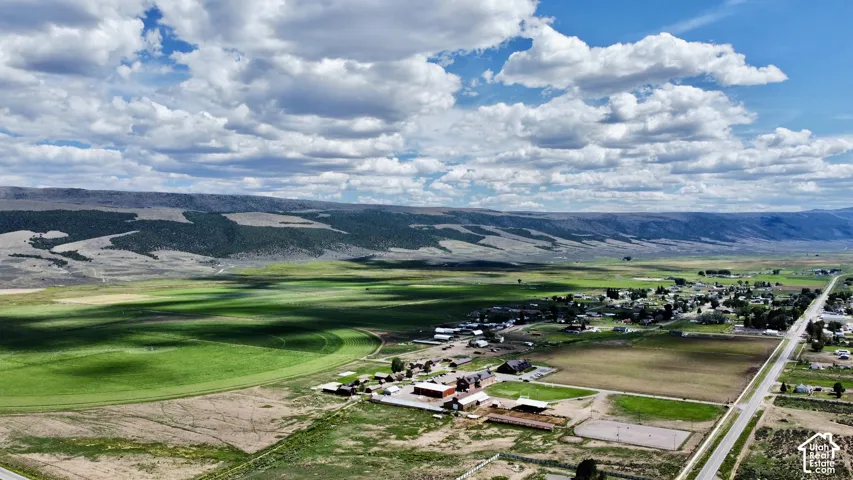Expansive rural landscape featuring green fields, distant mountains, and a clear sky with clouds