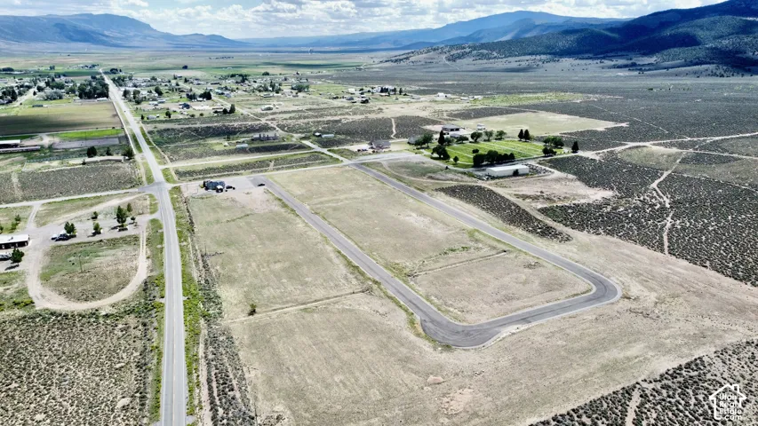 Expansive aerial encompassing multiple land parcels, paved roadways, and a distant town, set against a backdrop of mountains