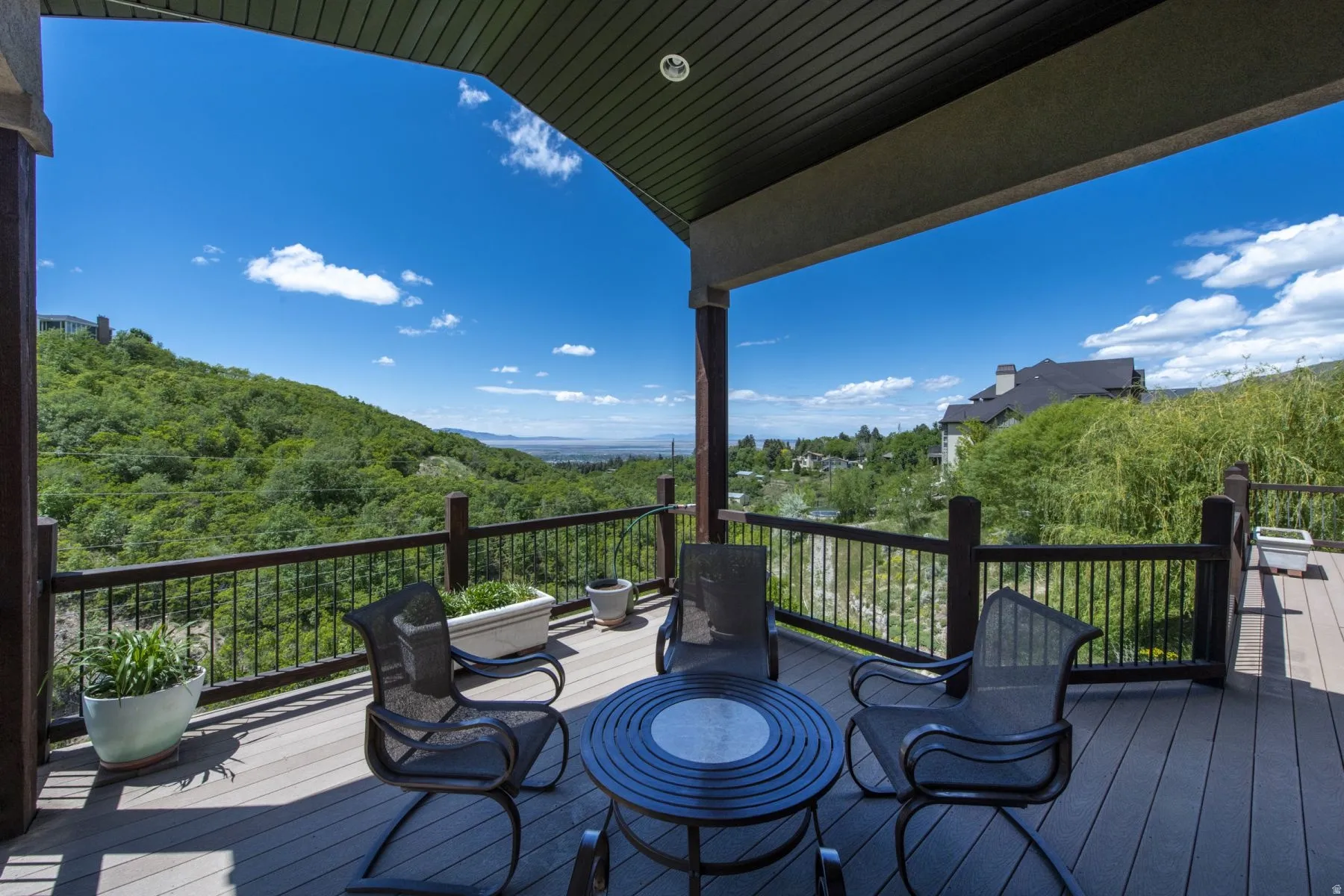 Covered deck with metal railing overlooking verdant hillside landscape and distant mountain backdrop