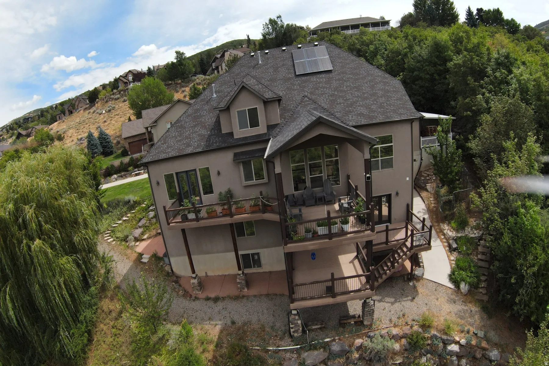 Multi-level deck and balcony system, solar panel array, dormer window, extensive exterior fenestration, and natural rock landscaping