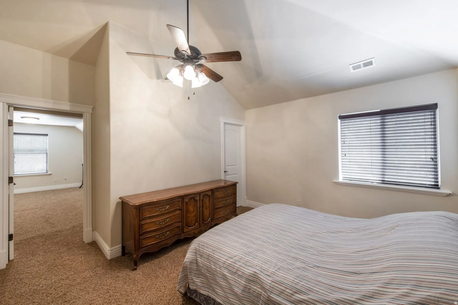 Carpeted room featuring a sloped ceiling, ceiling fan with integrated lighting, and a window with blinds