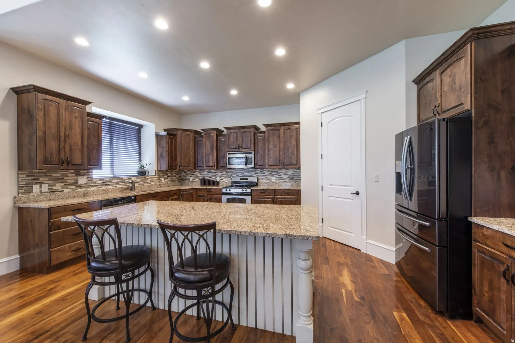 Spacious kitchen featuring rich wood cabinetry, granite countertops, a tiled backsplash, wood-finish flooring, and recessed lighting