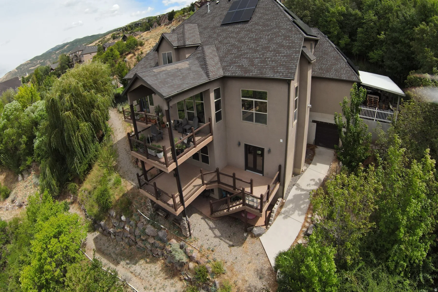 Multi-level exterior decks with dark wood railings, mature landscaping, concrete walkway, and solar panels