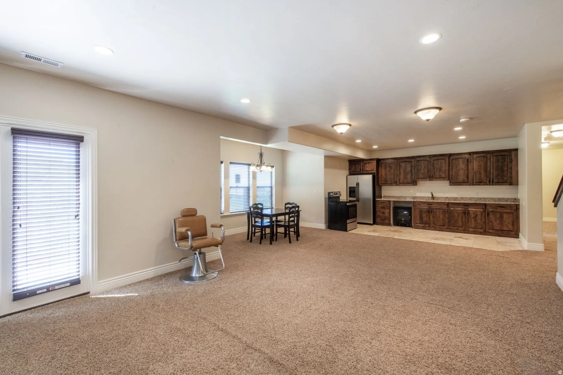 Recessed lighting, wood-finish cabinetry, built-in stainless steel appliances, tiled wet bar area, and neutral carpeting