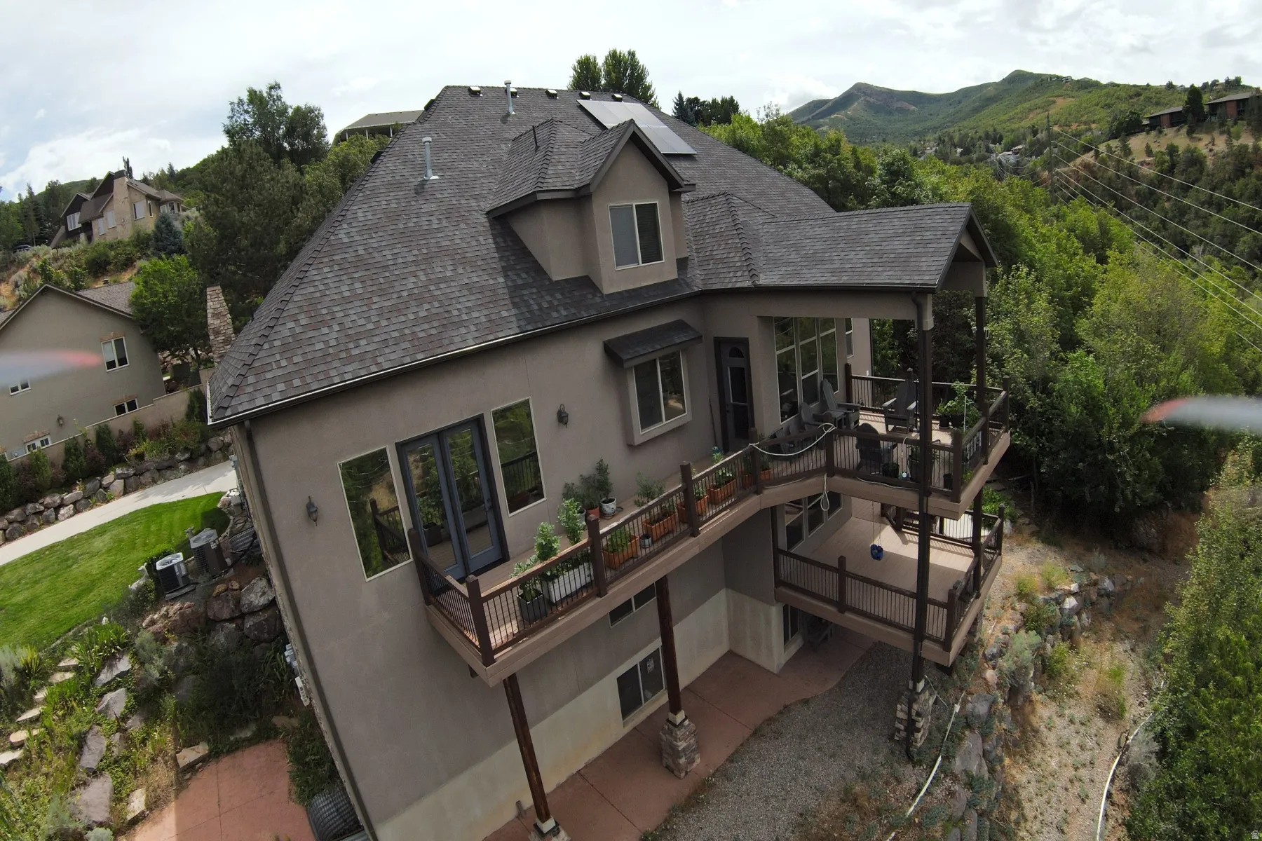 Multi-level exterior decks, shingle roof, solar panels, stucco siding, and surrounding natural landscape