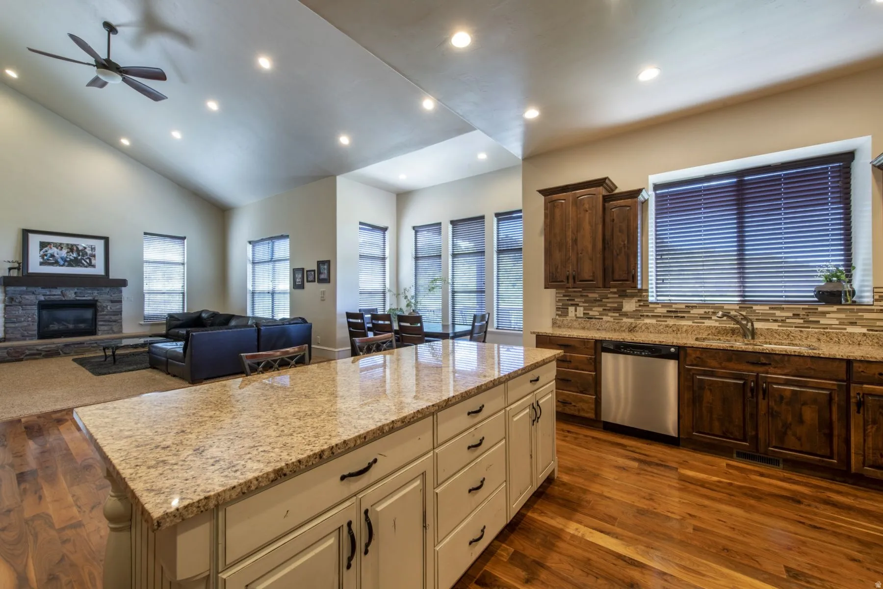 Kitchen island with a light-colored countertop, wood-finish flooring, dark wood cabinetry, a mosaic tile backsplash, and a stainless steel dishwasher
