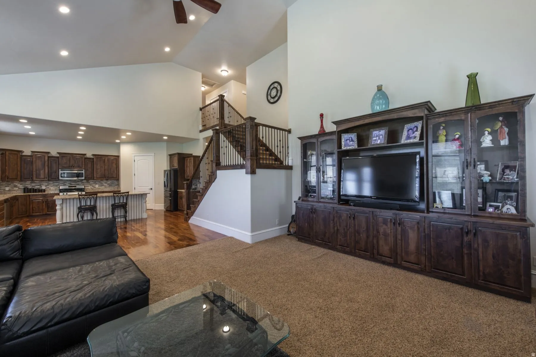 Expansive open-concept living area featuring a built-in entertainment center, a grand staircase with decorative railing, and recessed lighting