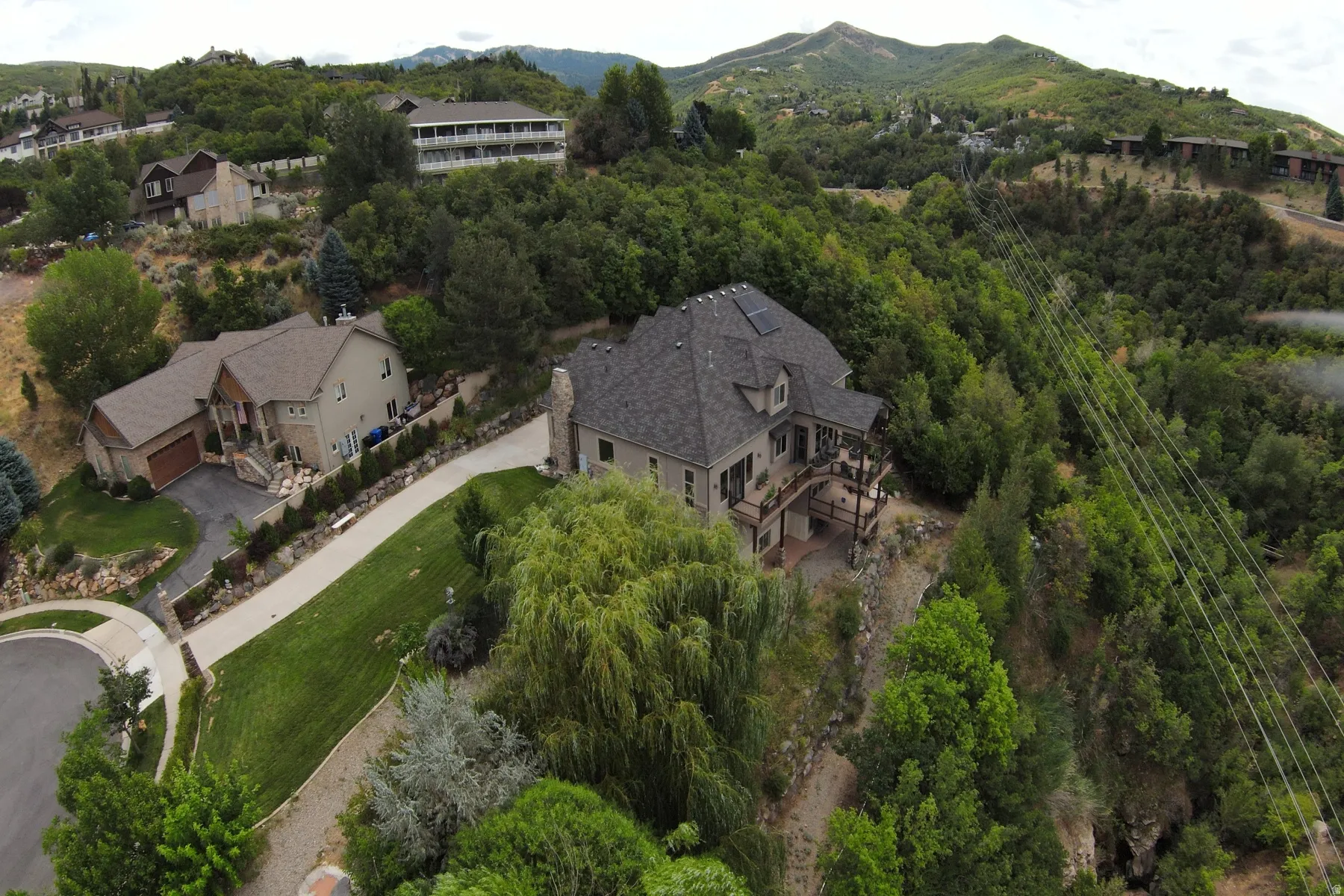 Expansive terraced property with a multi-level deck, surrounding mature trees, and mountainous backdrop